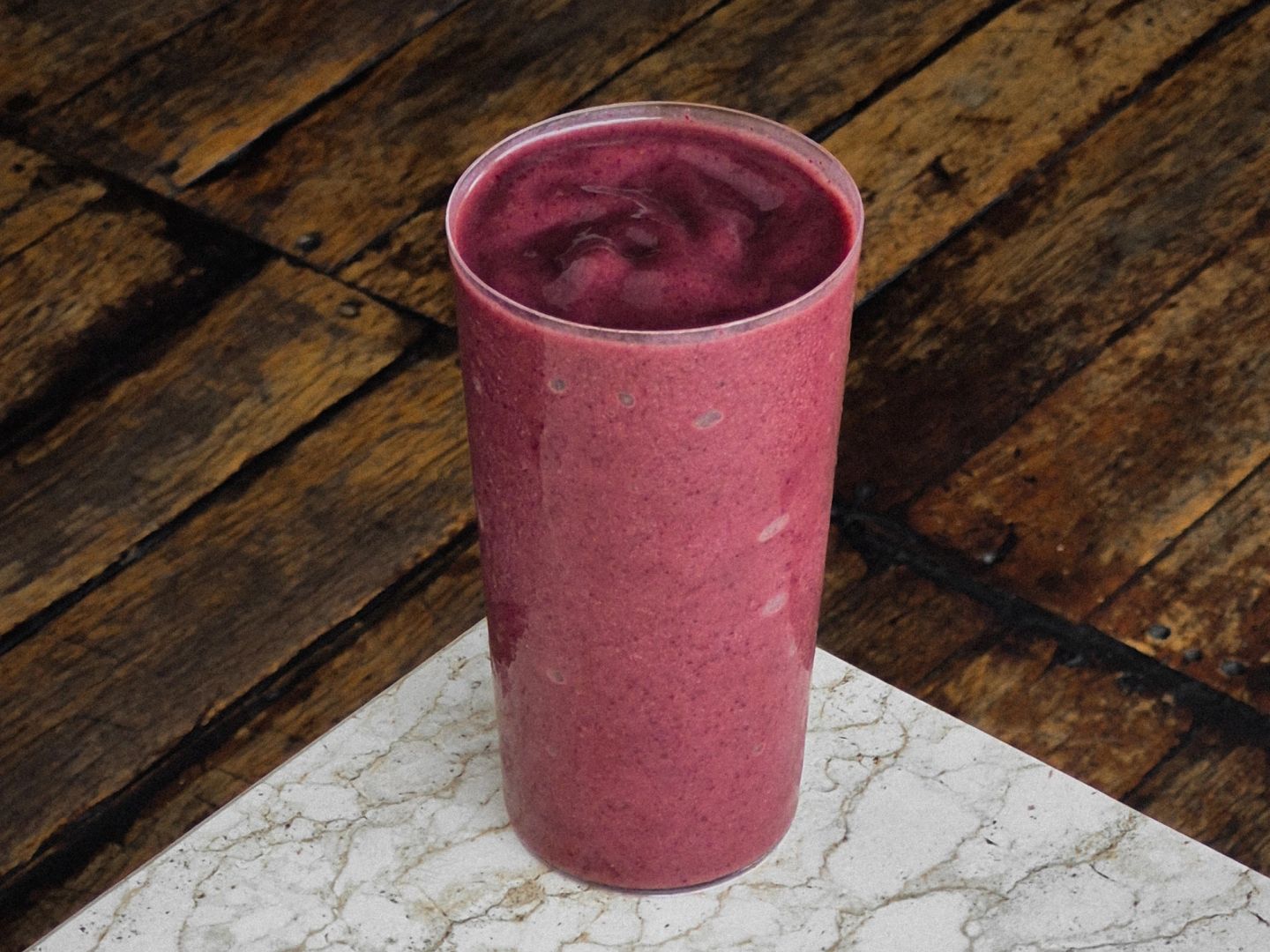 Deep purple-red acai smoothie in a tall glass on a marble surface.