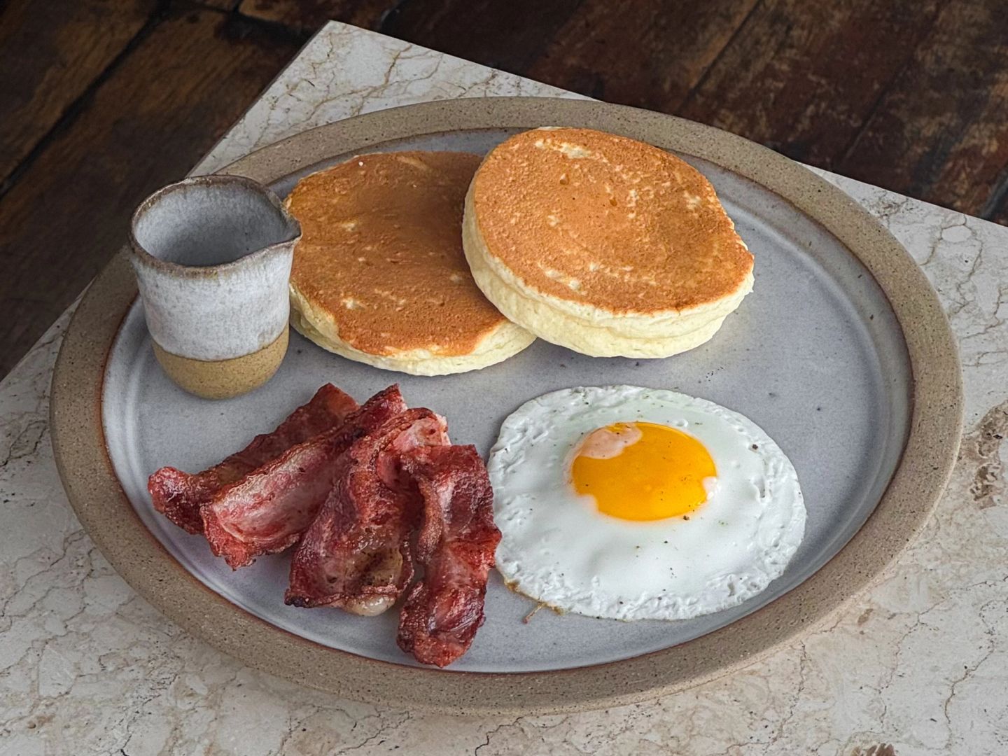 fluffy hotcakes with honey, fried egg and crispy bacon on top of a white marble table 