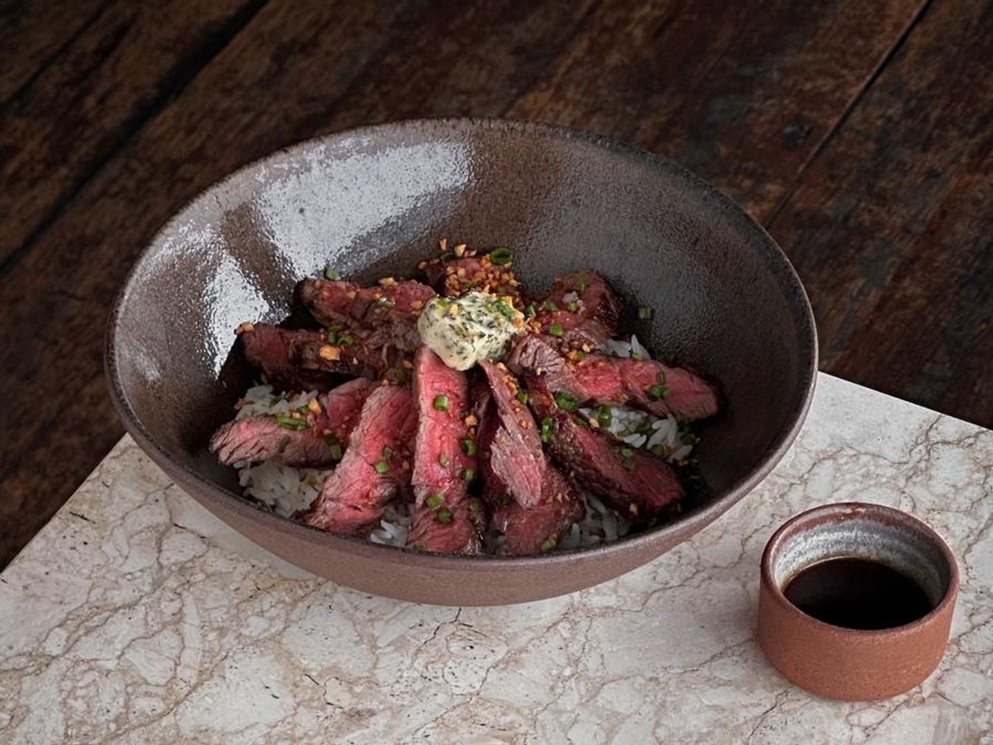 Sliced steak over rice topped with herb butter, served with a dipping sauce.