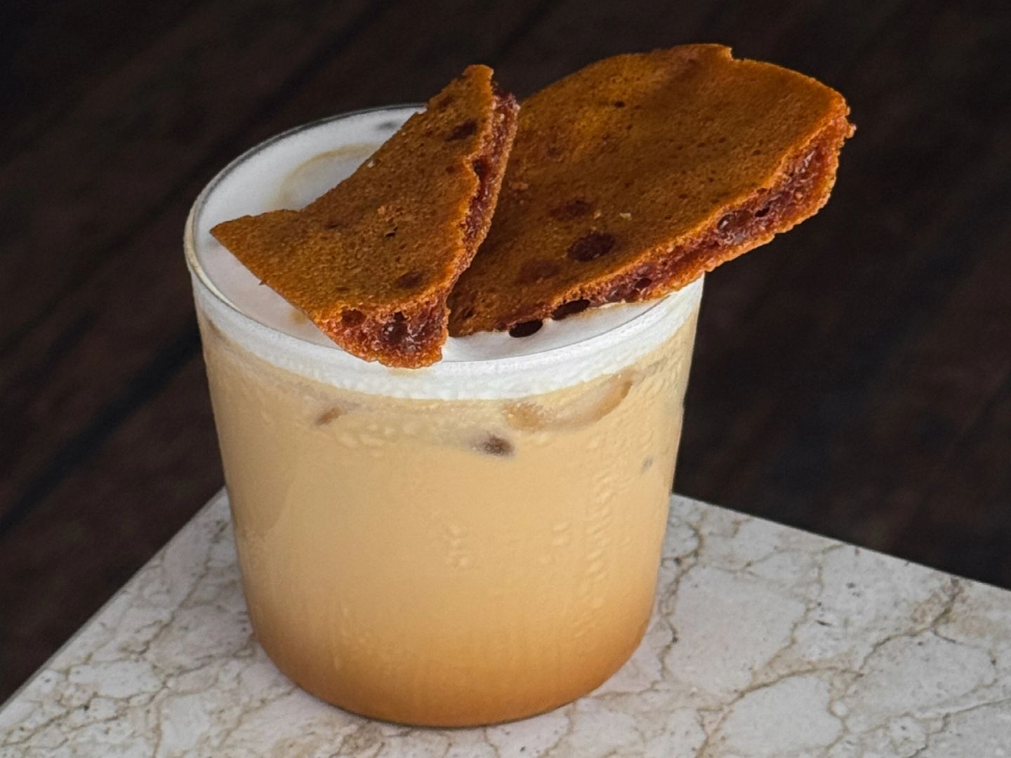 Iced latte topped with foam and two shards of caramel brittle.
