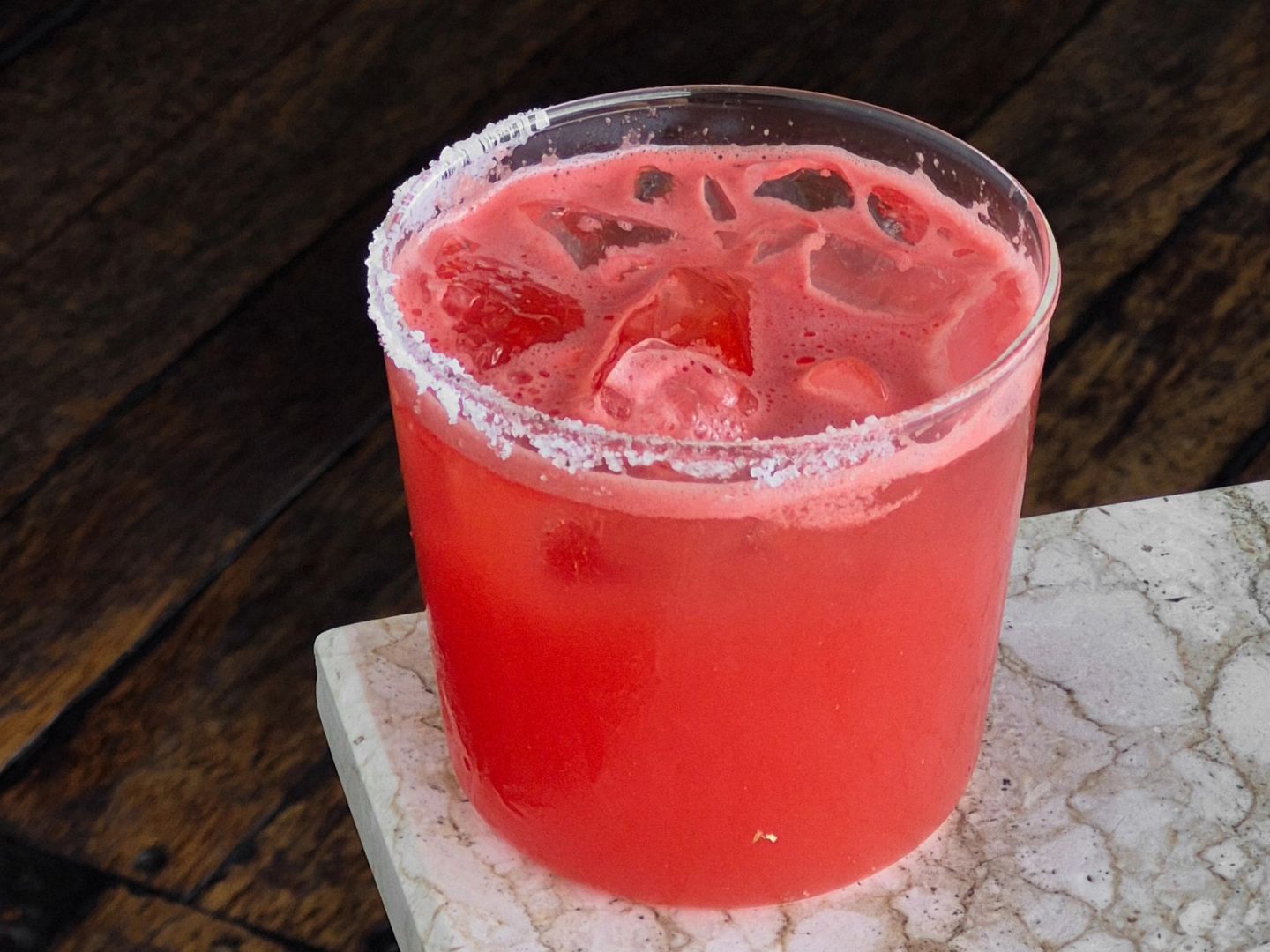 Iced watermelon-red drink over ice in a salt-rimmed glass.