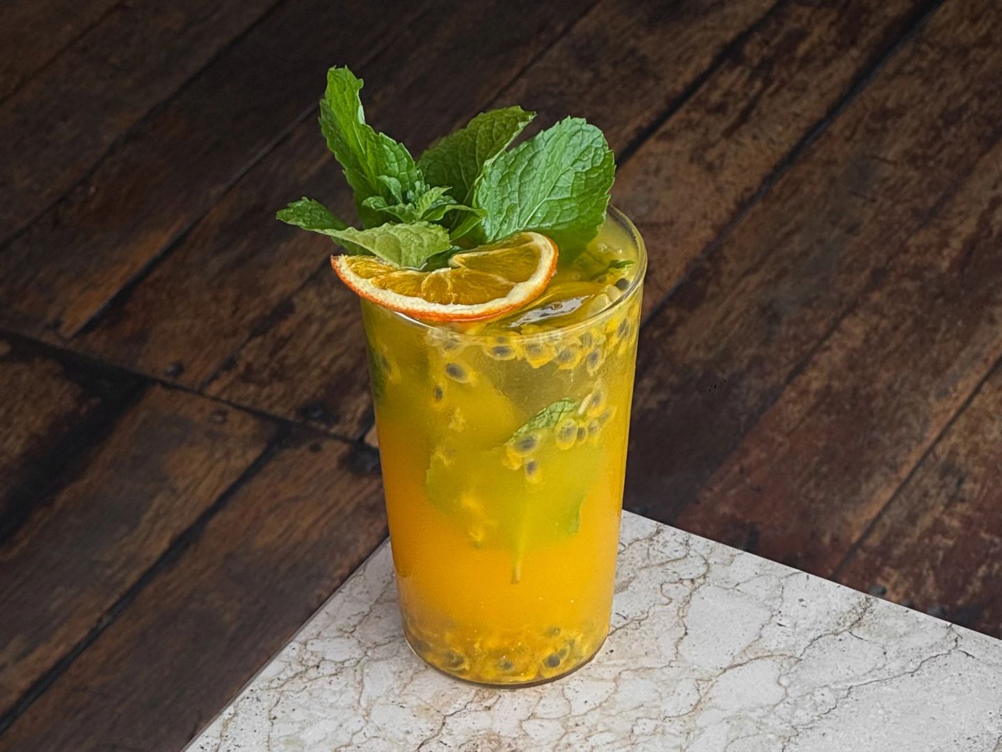 Bright orange passionfruit drink garnished with mint, a dried orange slice, and lime over ice.