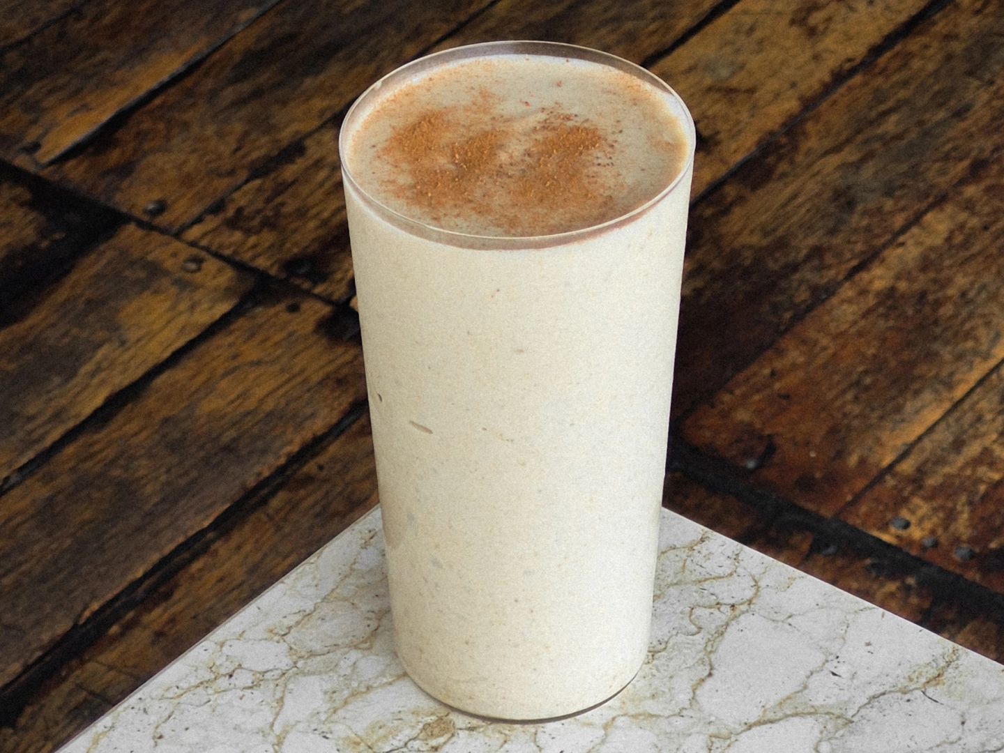 Creamy banana and peanut butter smoothie dusted with cinnamon in a tall glass.