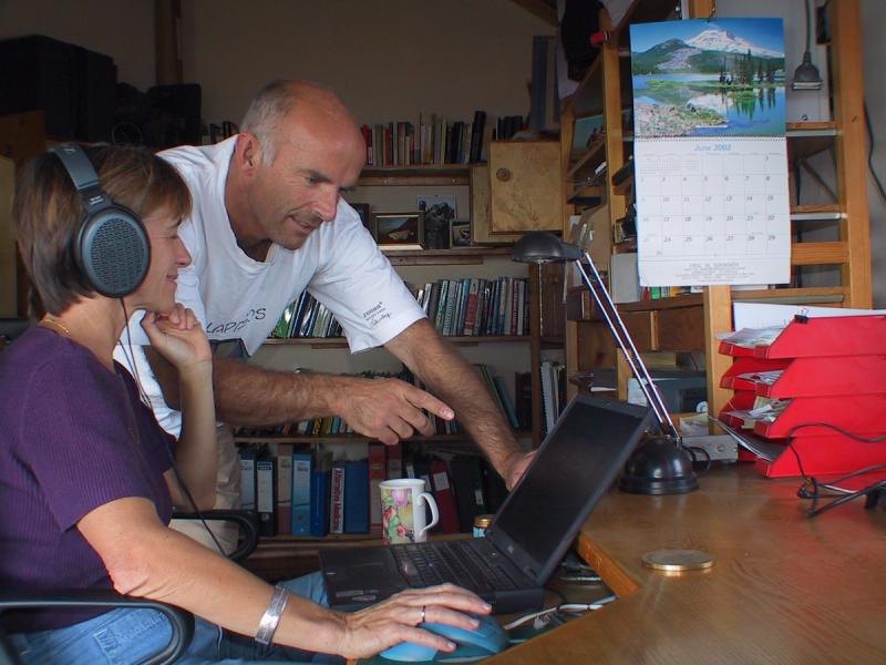 Petter Granli points to a laptop screen while a Joyce wearing headphones operates it at a desk in an office with bookshelves.