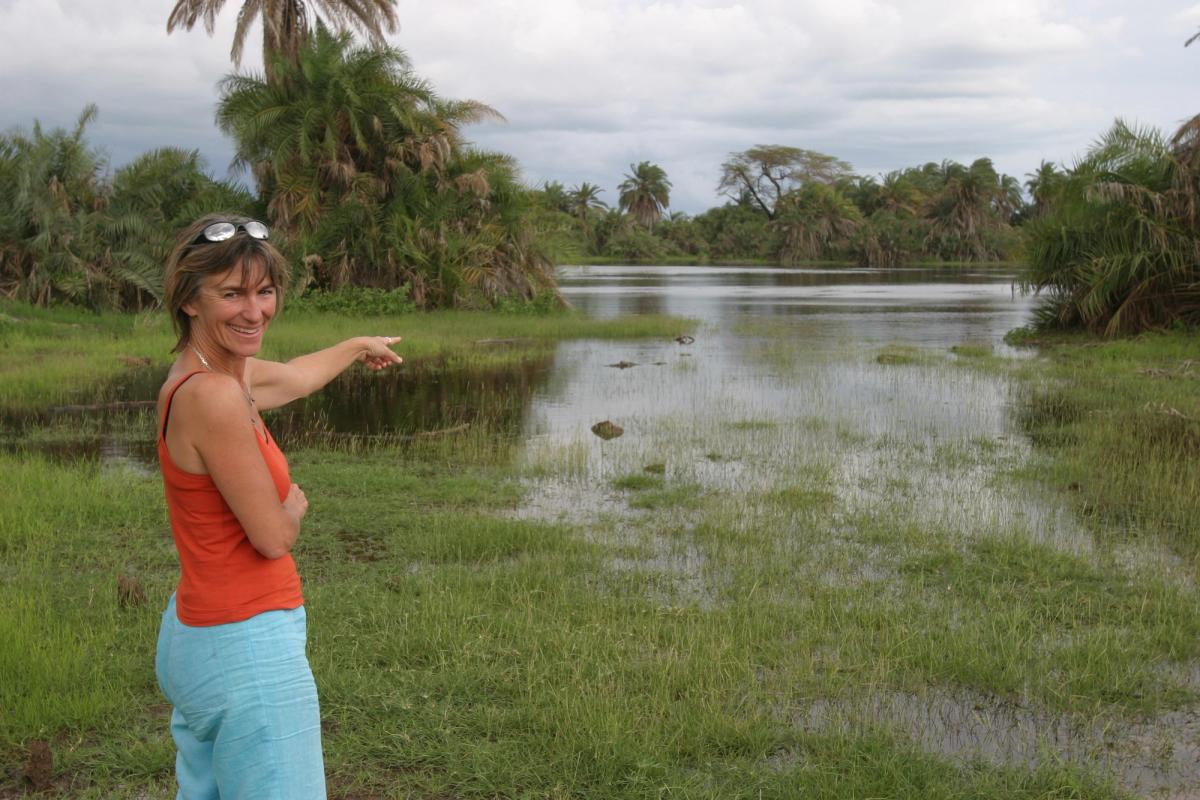 Smiling woman points at crocodiles in a tropical marsh with palm trees.