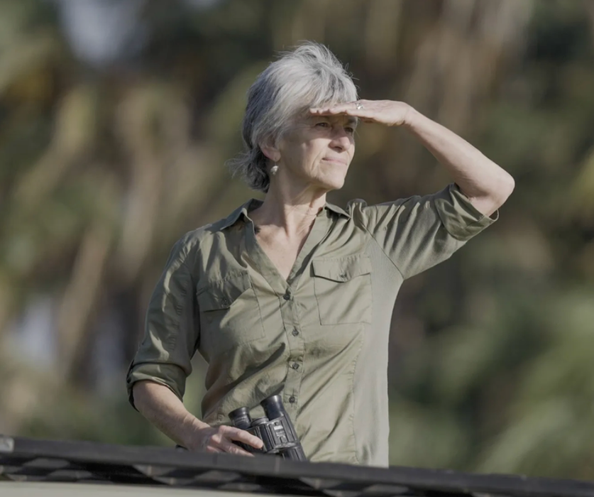 Woman with binoculars shielding her eyes while looking into the distance.