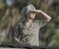 Woman with binoculars shielding her eyes while looking into the distance.