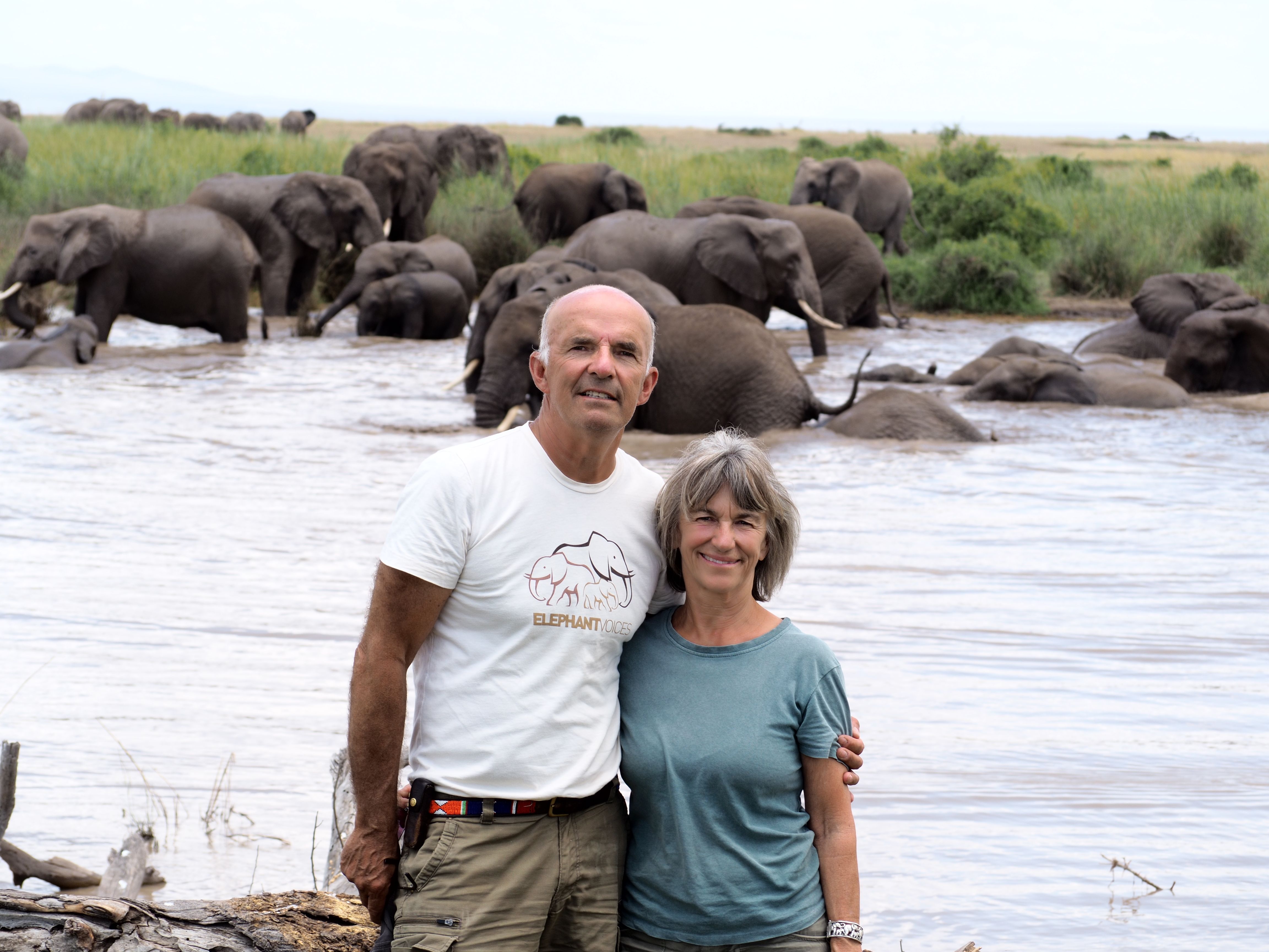 Petter Granli and Joyce Poole in Amboseli National Park with elephants bathing and playing in the background.