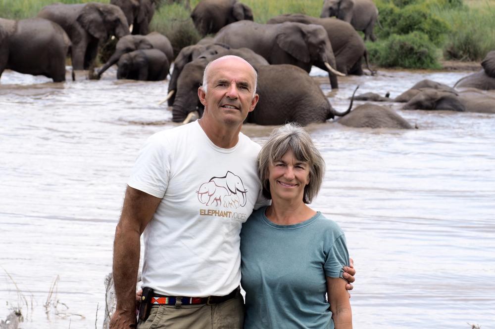 Petter Granli and Joyce Poole in Amboseli National Park with elephants bathing and playing in the background.