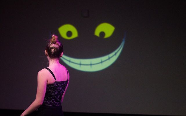 A photograph from the interactive dance performance.  A project visual of  Cheshire Cat hidden in the shadows,  looks and follows the dancer.