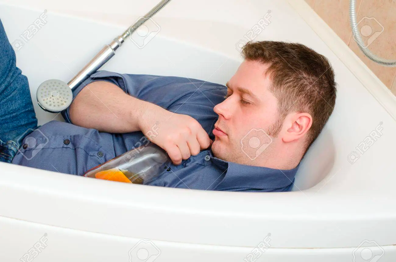 Stock image of a white man asleep in a bathtub clutching a beer bottle