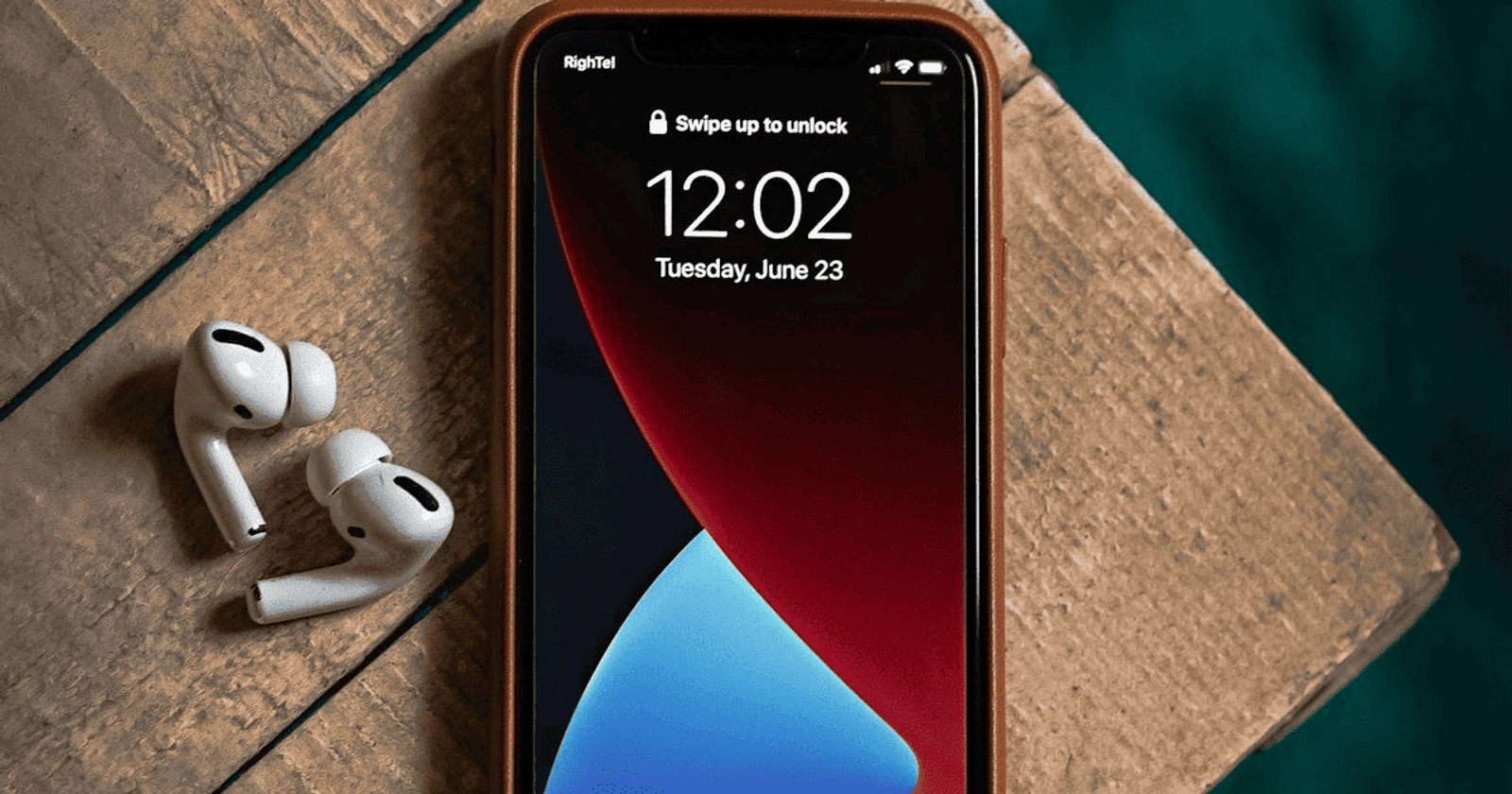 An iPhone lock screen showing the time before the phone is unlocked, resting on a wooden block beside a pair of wireless earbuds
