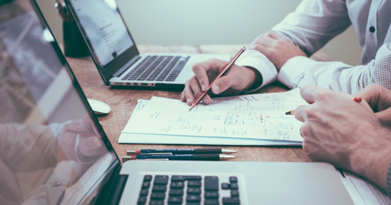 Two people reviewing a printed project document with pens and laptops on a desk, working through a vendor evaluation before signing
