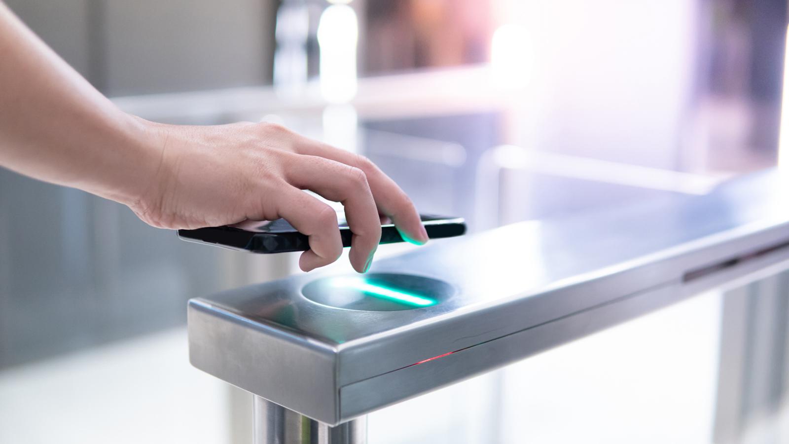 hand holding a smartphone to a scanner to open gate at cashierless retail location