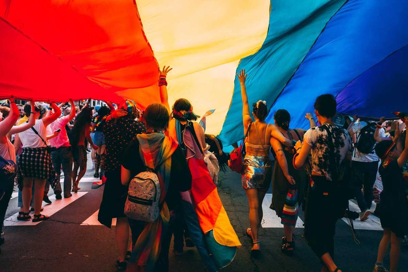 People walking under a gigantic flag during the annual Pride parade