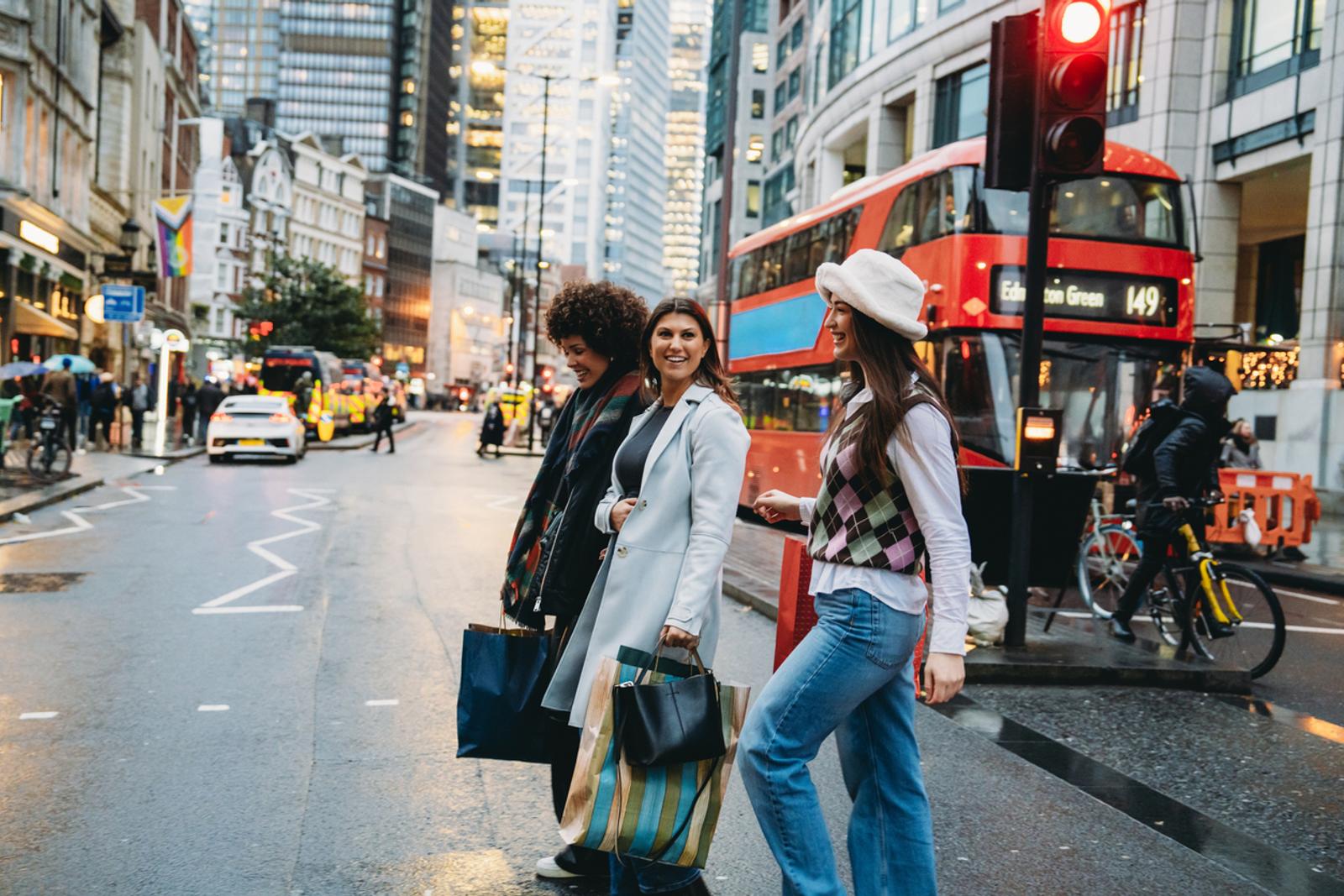 Three young women walking on crosswalk in london with shopping bags