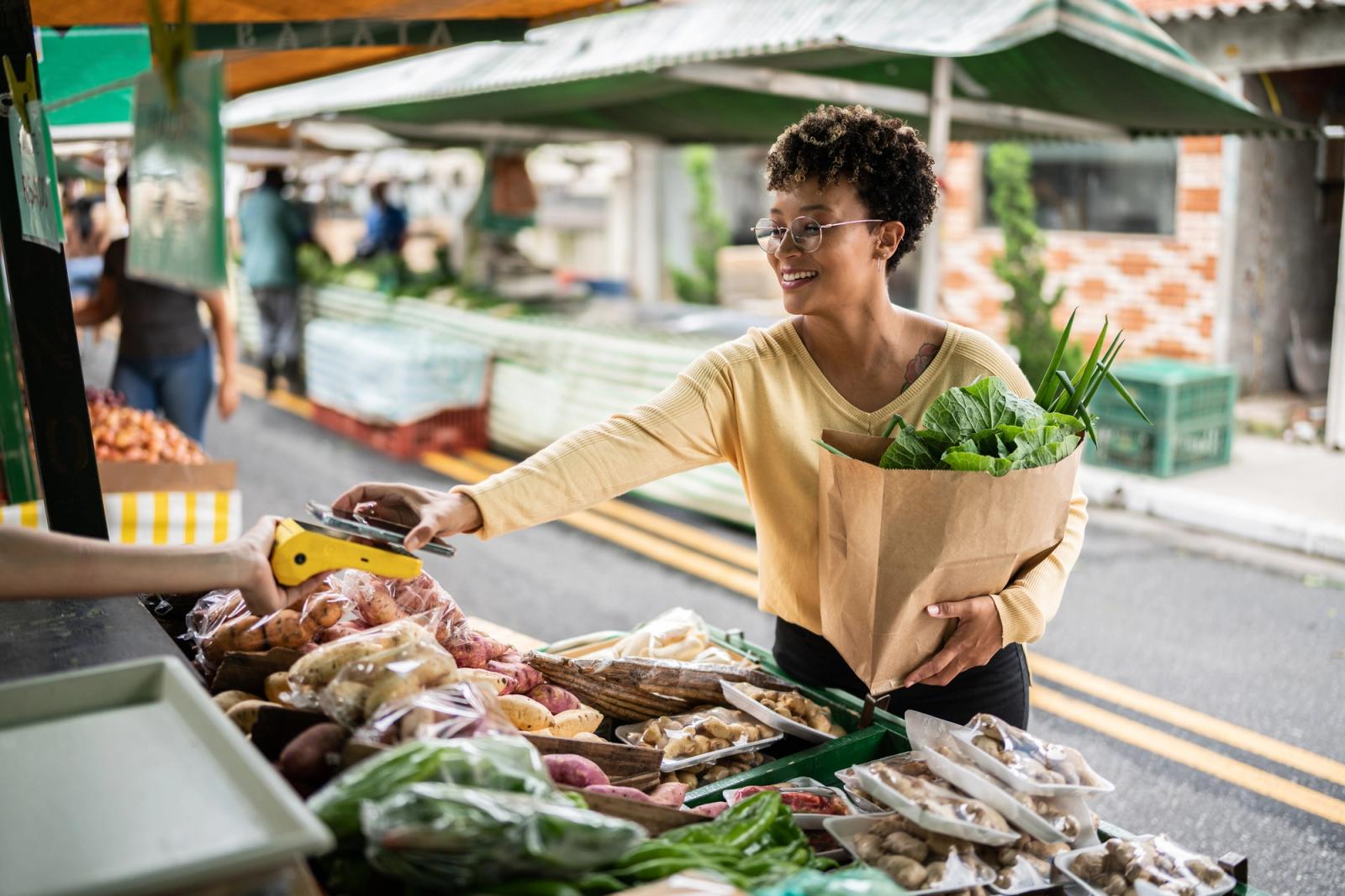 Young woman paying with mobile phone at a street market
