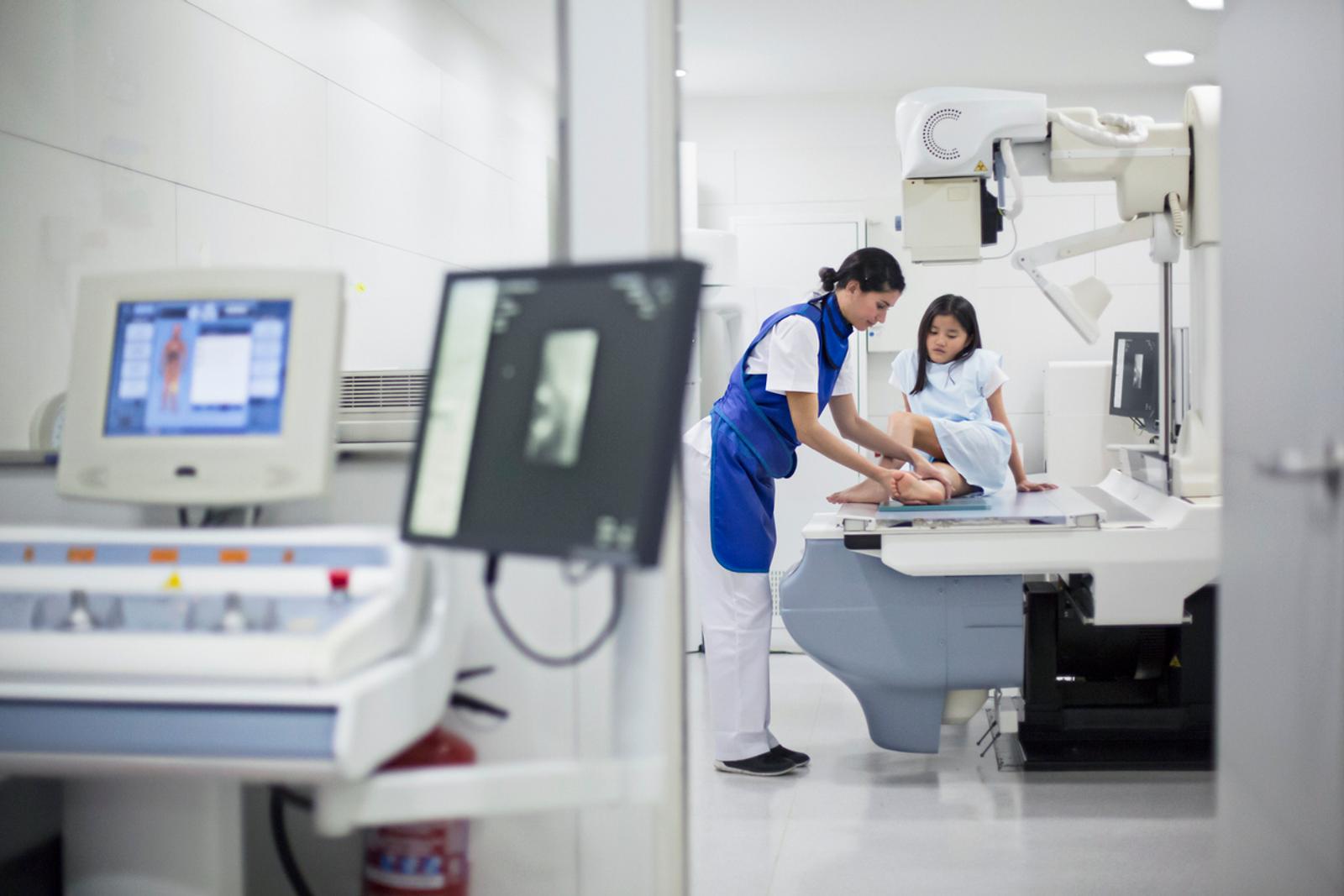 An x-ray technician preparing to scan a young woman's leg in the background with medical devices blurred in the foreground