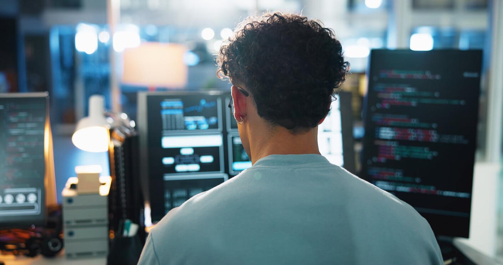 A developer sits in front of monitors at a desk