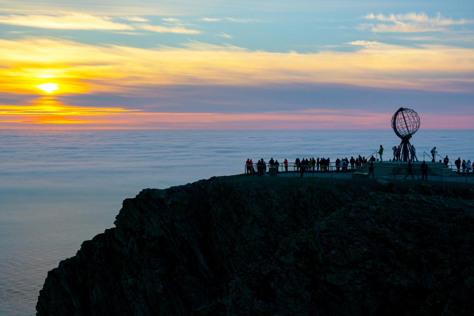 Tourist silhouettes, midnight sun and clouds at the North Cape