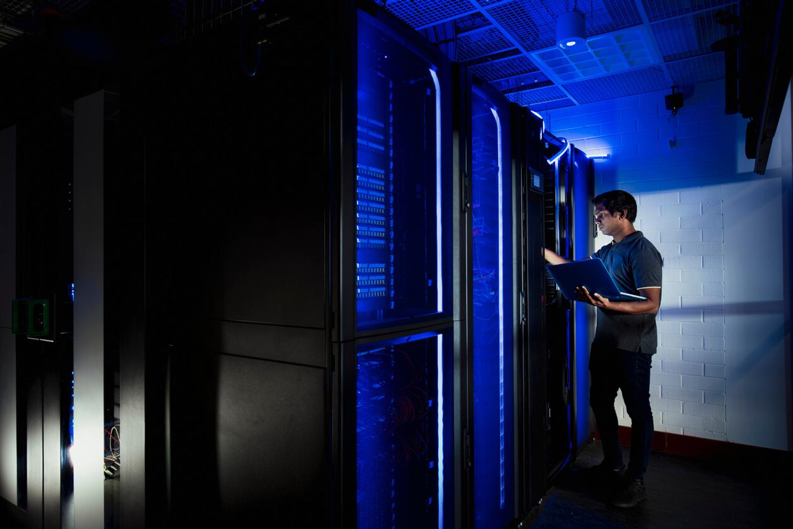 A young man works with a laptop in a server room