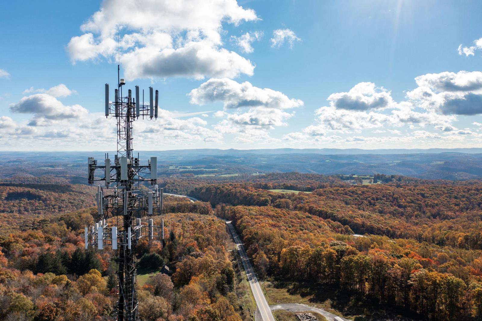 cellular tower in the forefront of the photo with trees and the sky