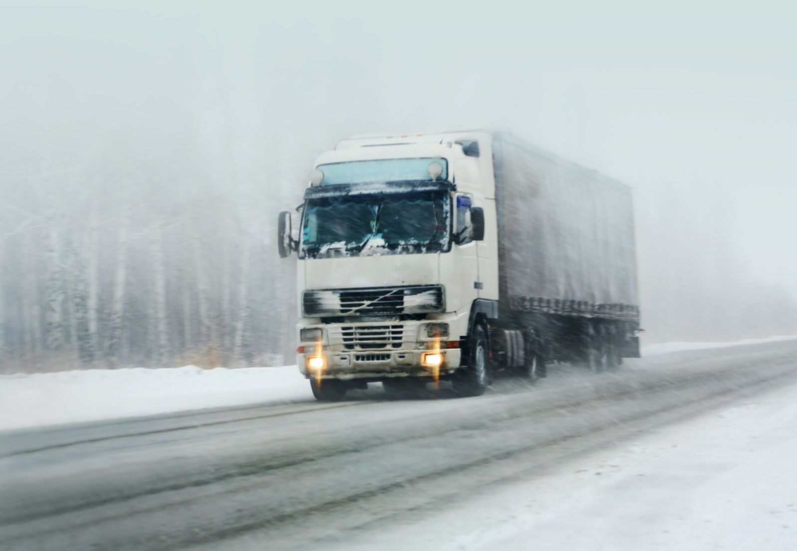 Freight truck driving on a winter road with snow falling down
