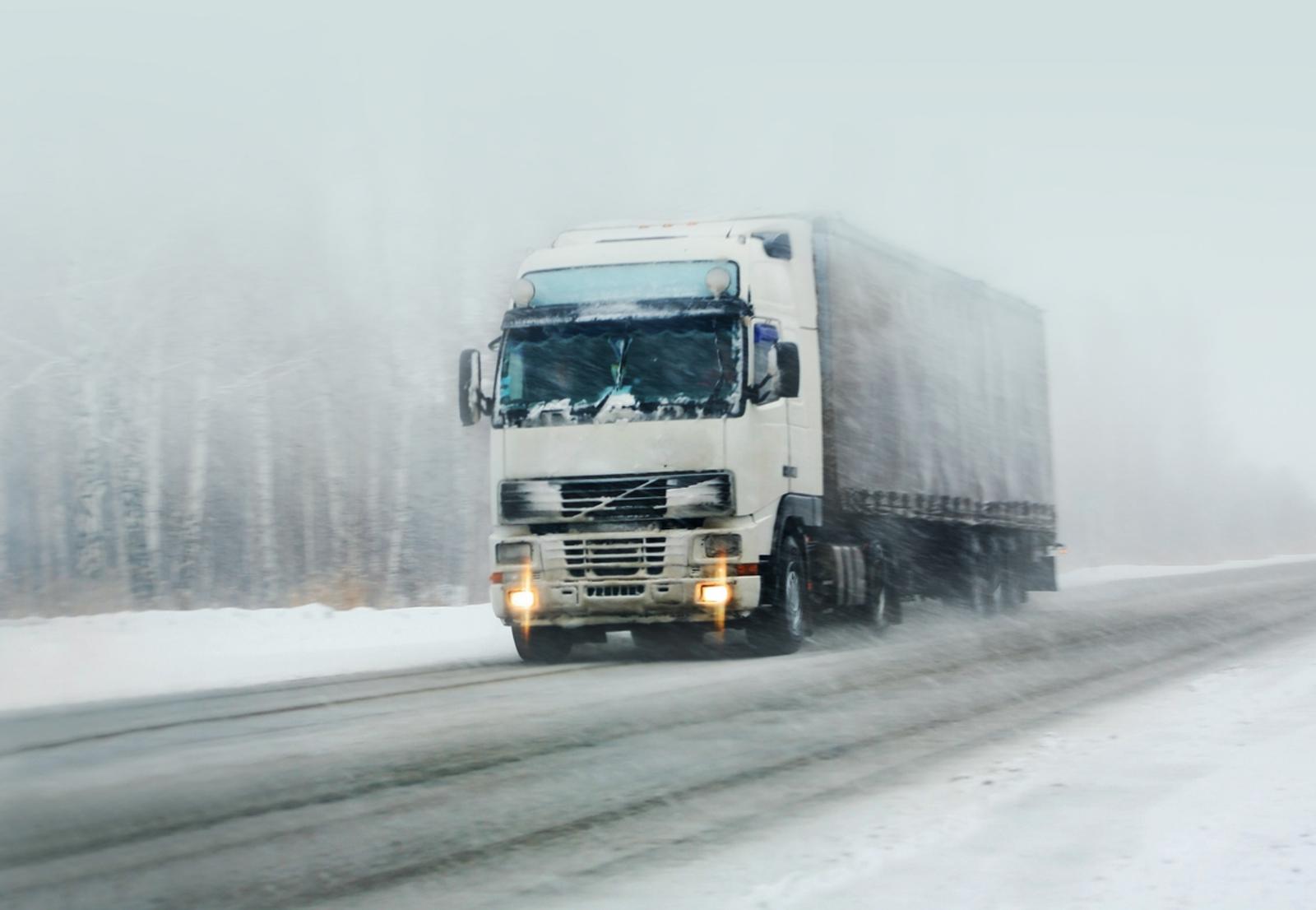Freight truck driving on a winter road with snow falling down