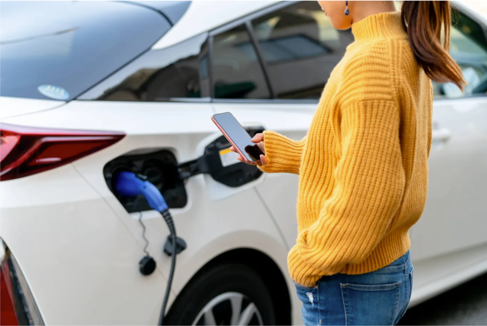 Woman in a yellow sweater charging their electric vehicle