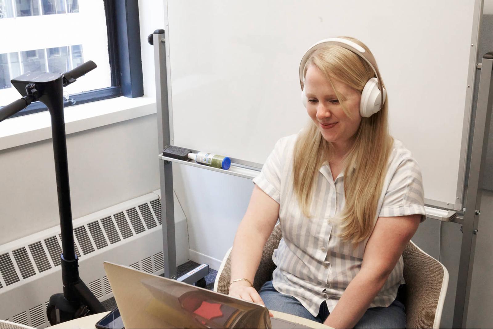 Woman sitting at a desk typing on a laptop computer wearing earphones