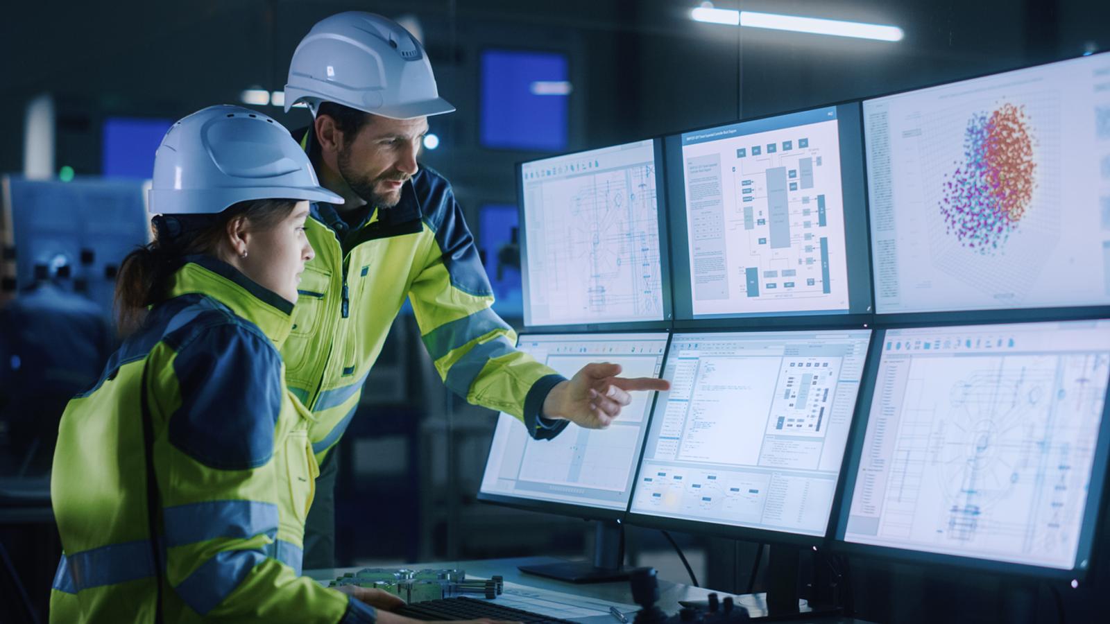 Two manufacturing team members review data on computer screens