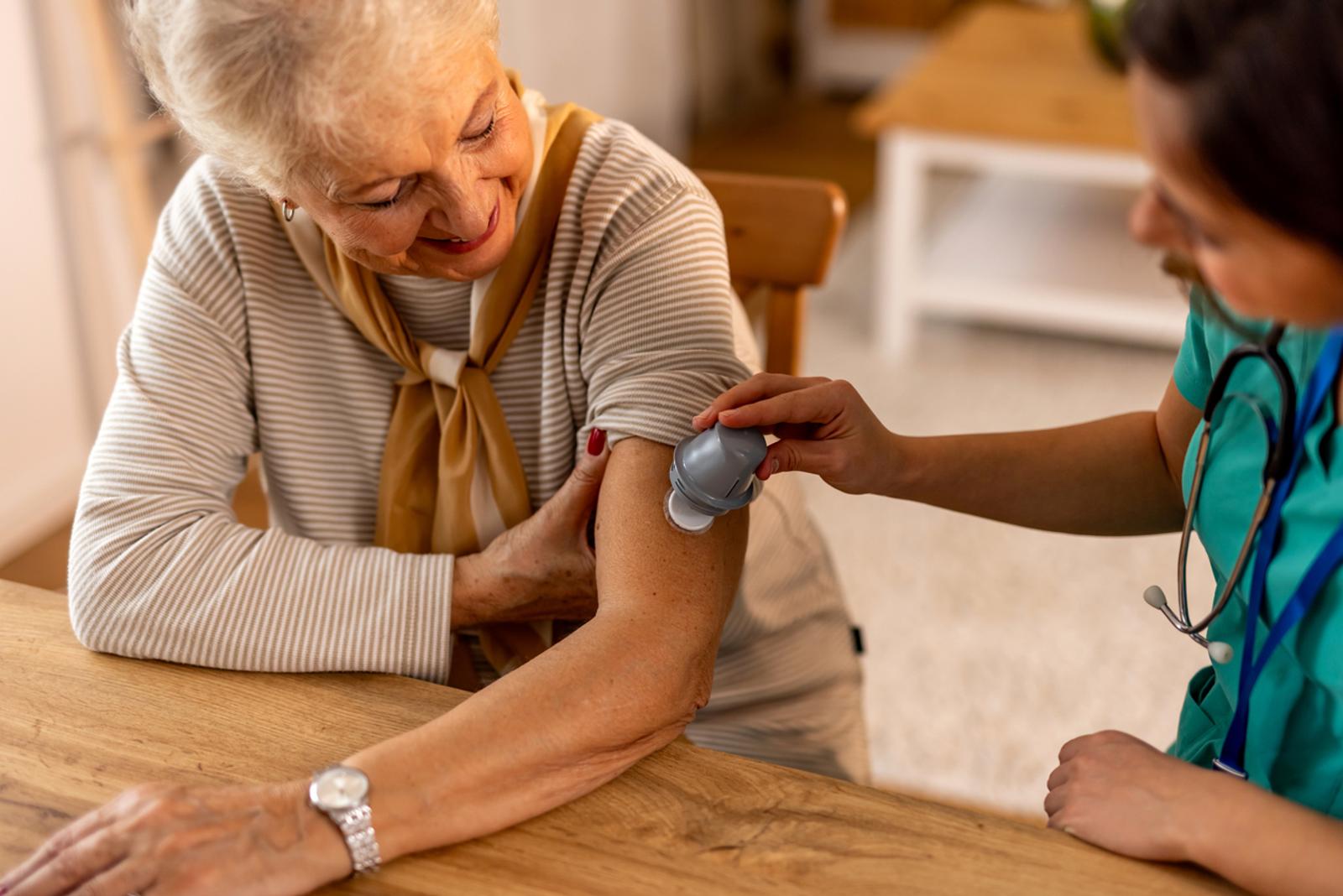 A healthcare professional applies a continuous glucose monitor to an older woman in her home.
