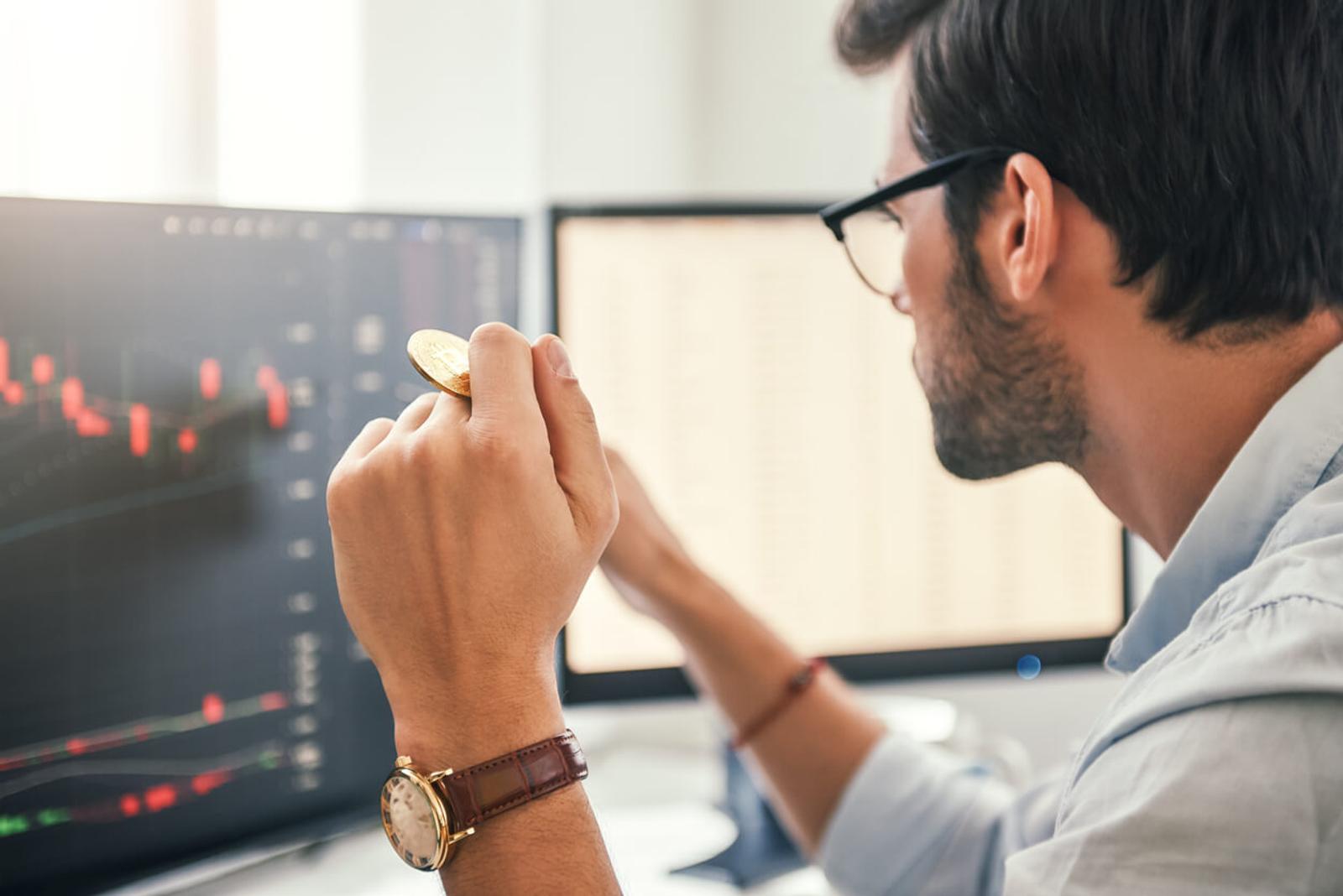 Trader holding Bitcoin in one hand while working his modern office.