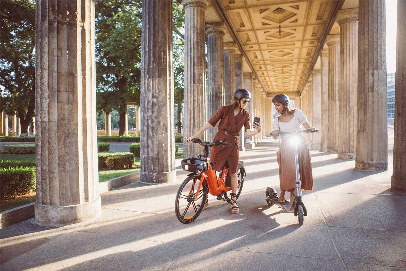 Two woman in Paris, France. One woman riding an e bike and another an e scooter looking at a phone.