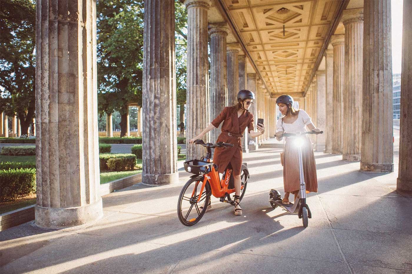 Two woman in Paris, France. One woman riding an e bike and another an e scooter looking at a phone.