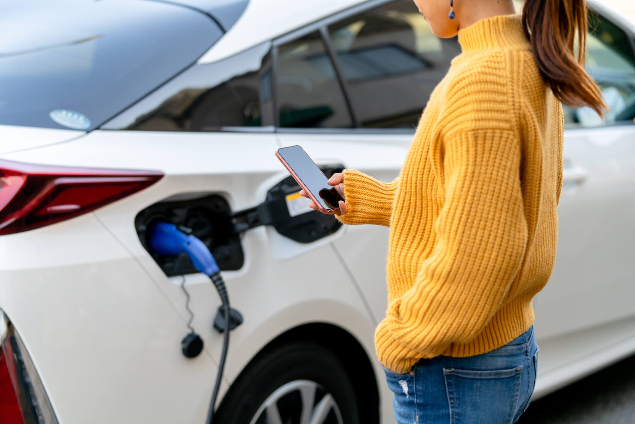 A woman in a yellow sweater uses her phone to pay for an EV charging station