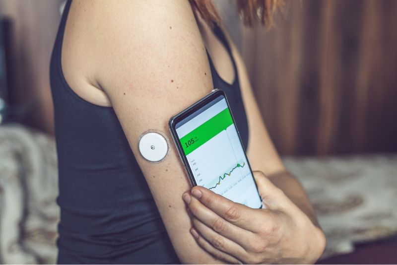 woman using a cell phone to track a health monitoring device on her arm