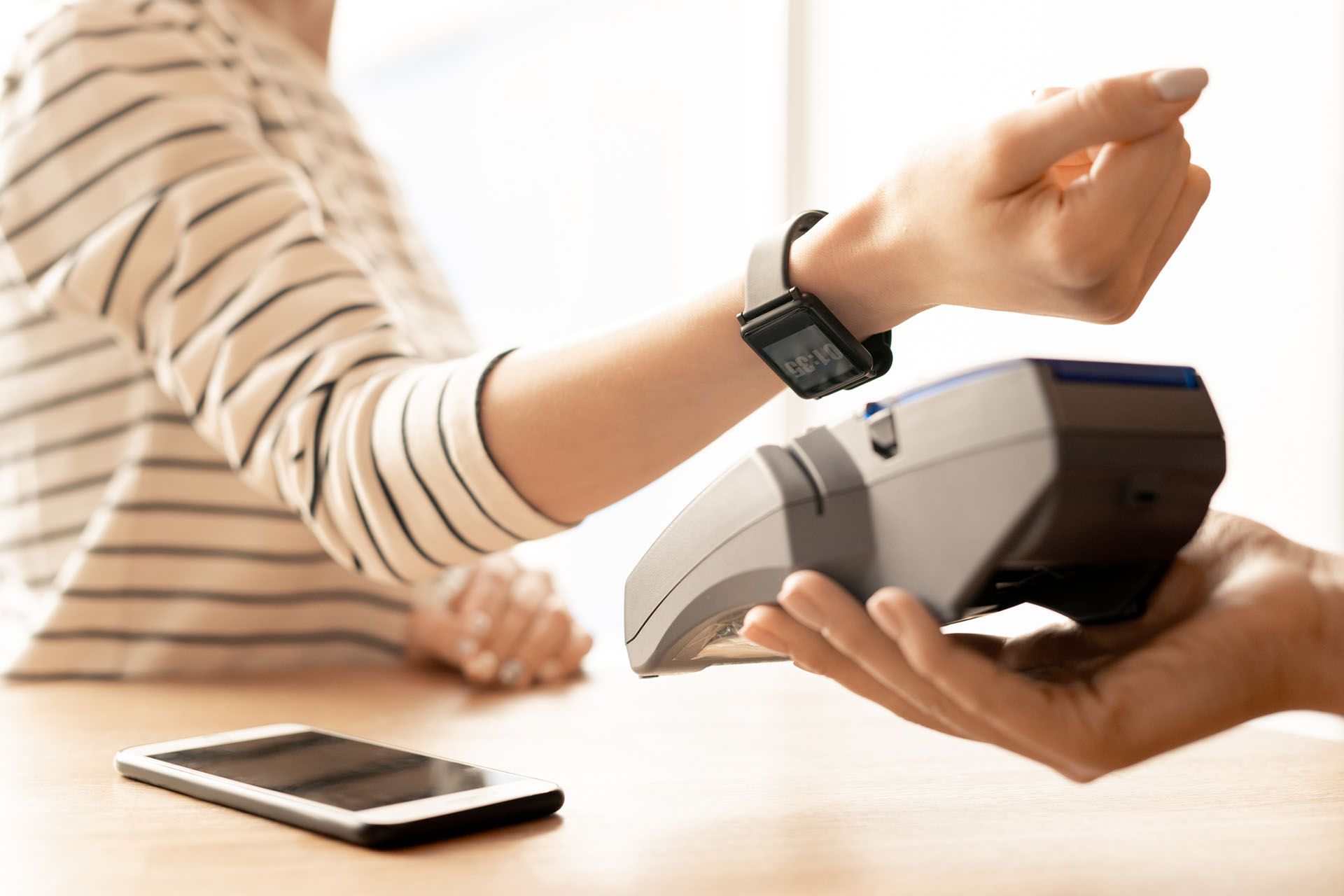 A person in a striped shirt uses their smart watch to pay at a retail point of sale.