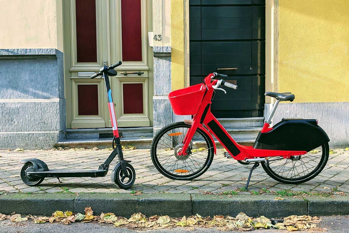 A scooter and e-bike are parked on a city sidewalk