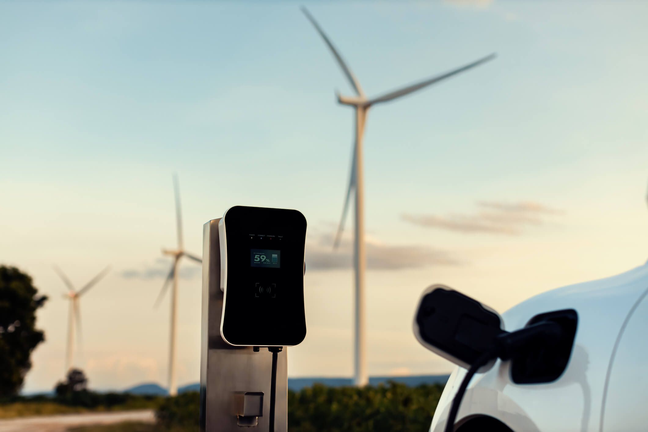 An electric car charges in the countryside near wind turbines