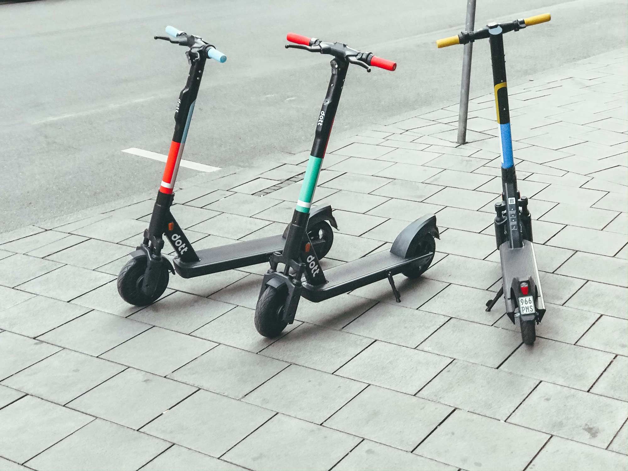 Three electric scooters on a sidewalk next to a street