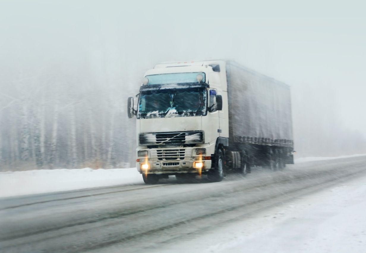 Freight truck driving on a winter road with snow falling down