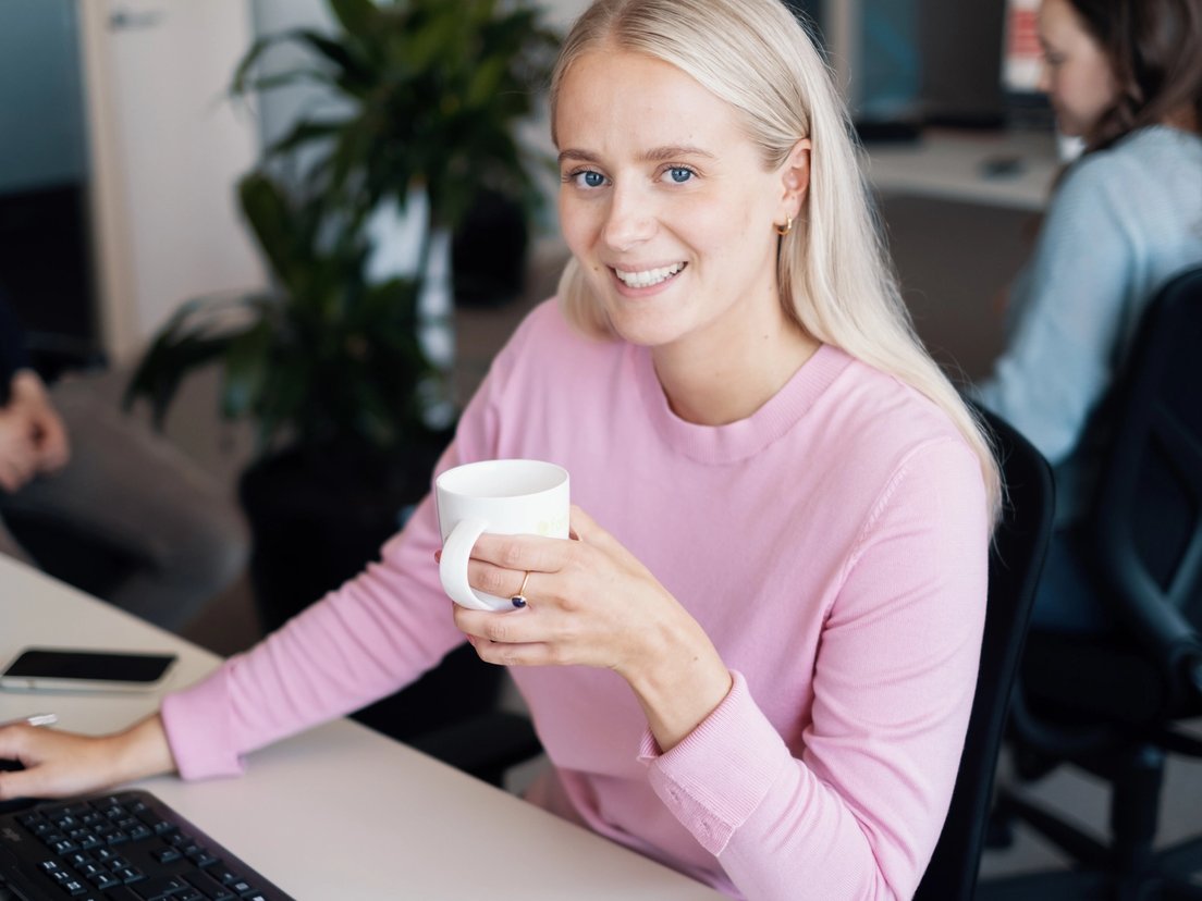 Smilende ung kvinne i rosa genser med kaffekopp. 