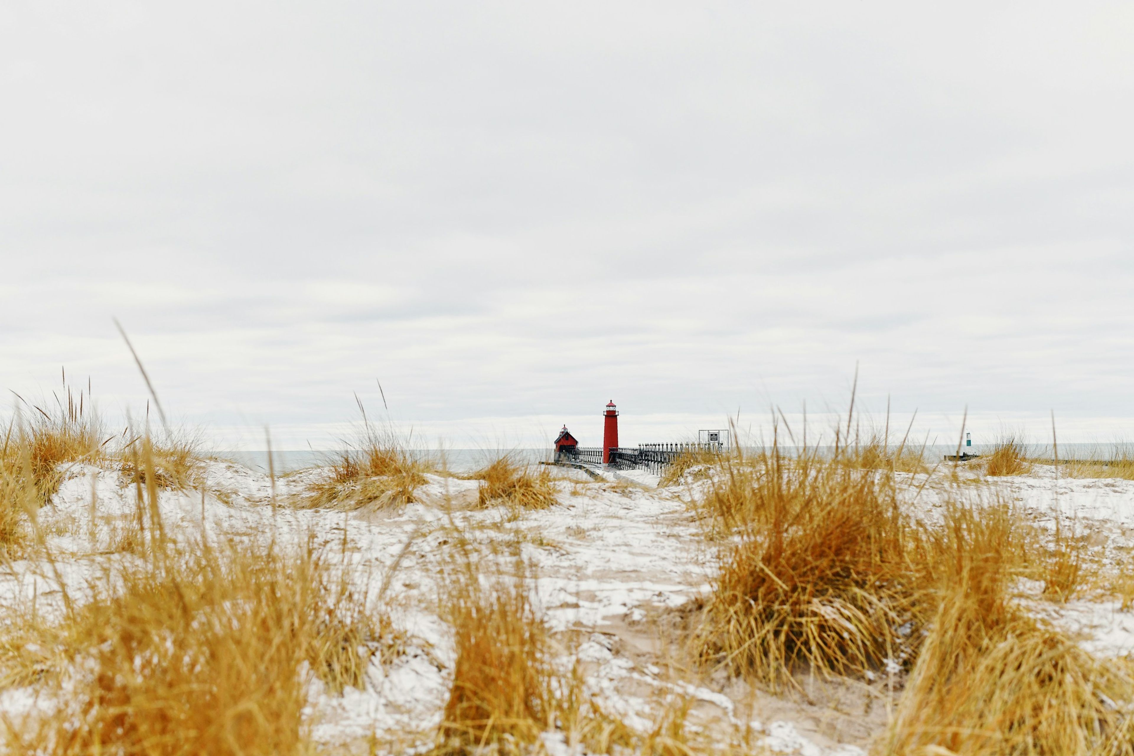 Red lighthouse beyond snowy dune grass