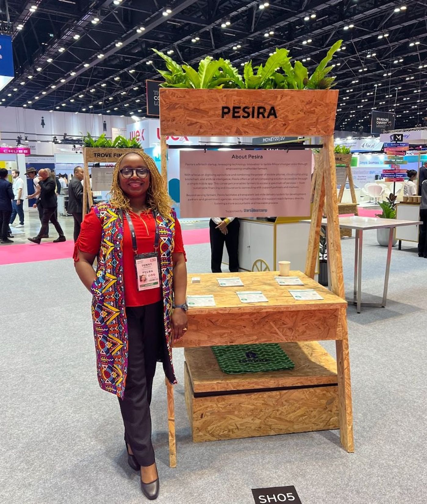 Someone at the Pesira stand at a trade show, beside a board about the company