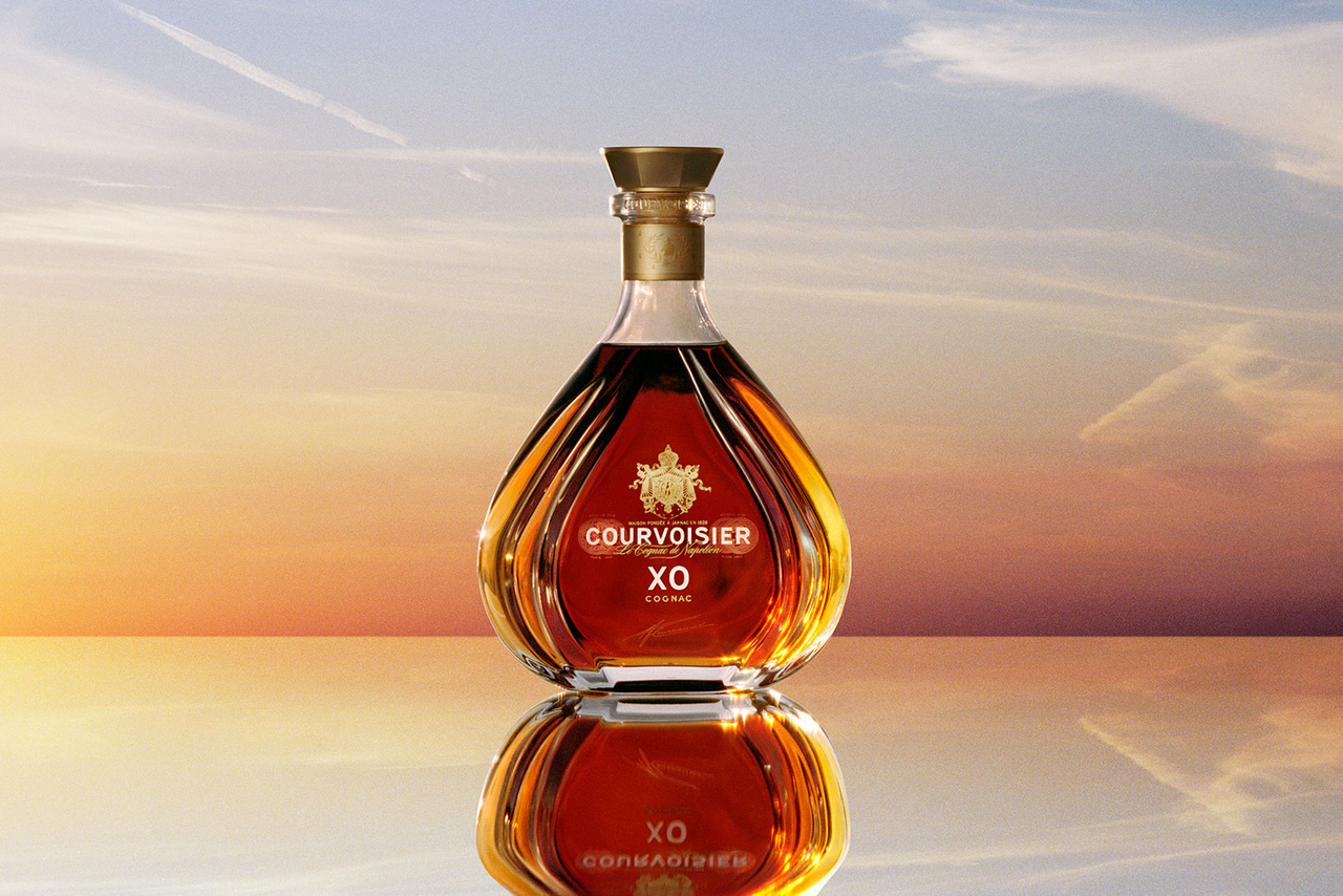 A decanter of Courvoisier XO Cognac against a sunset sky.