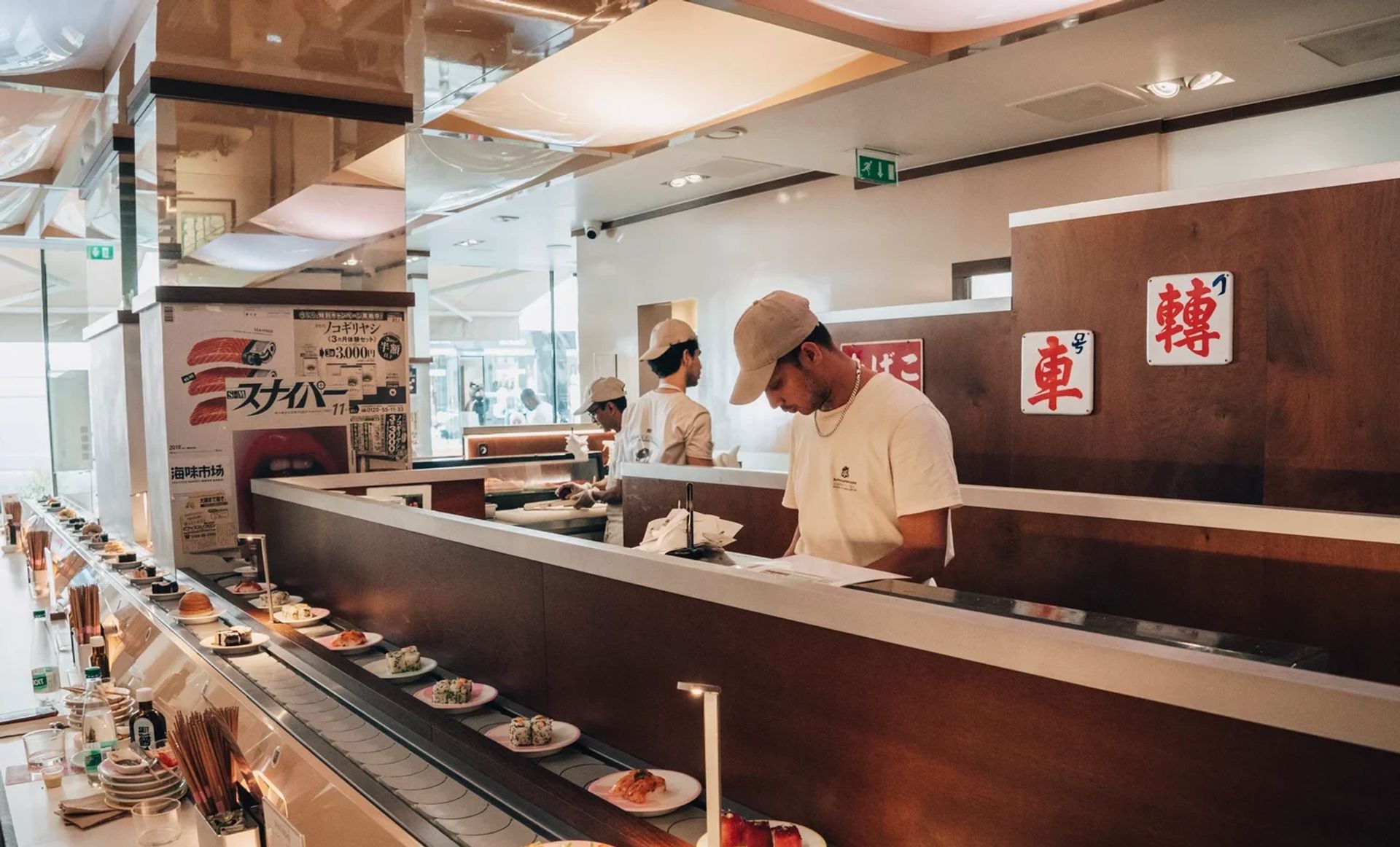Deux équipiers Matsuri en casquette derrière le comptoir tournant, assiettes de sushis en défilé