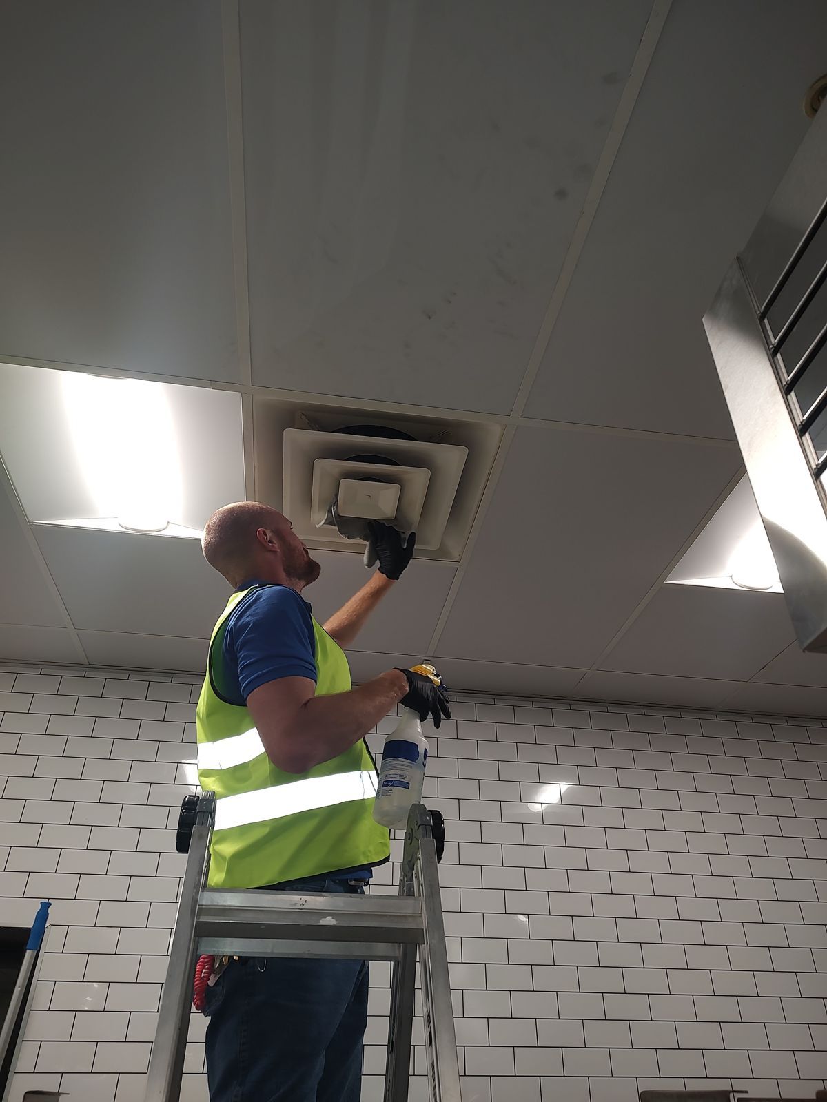 Crystal Clean crew member cleaning a ceiling air vent from a ladder during after-hours commercial cleaning