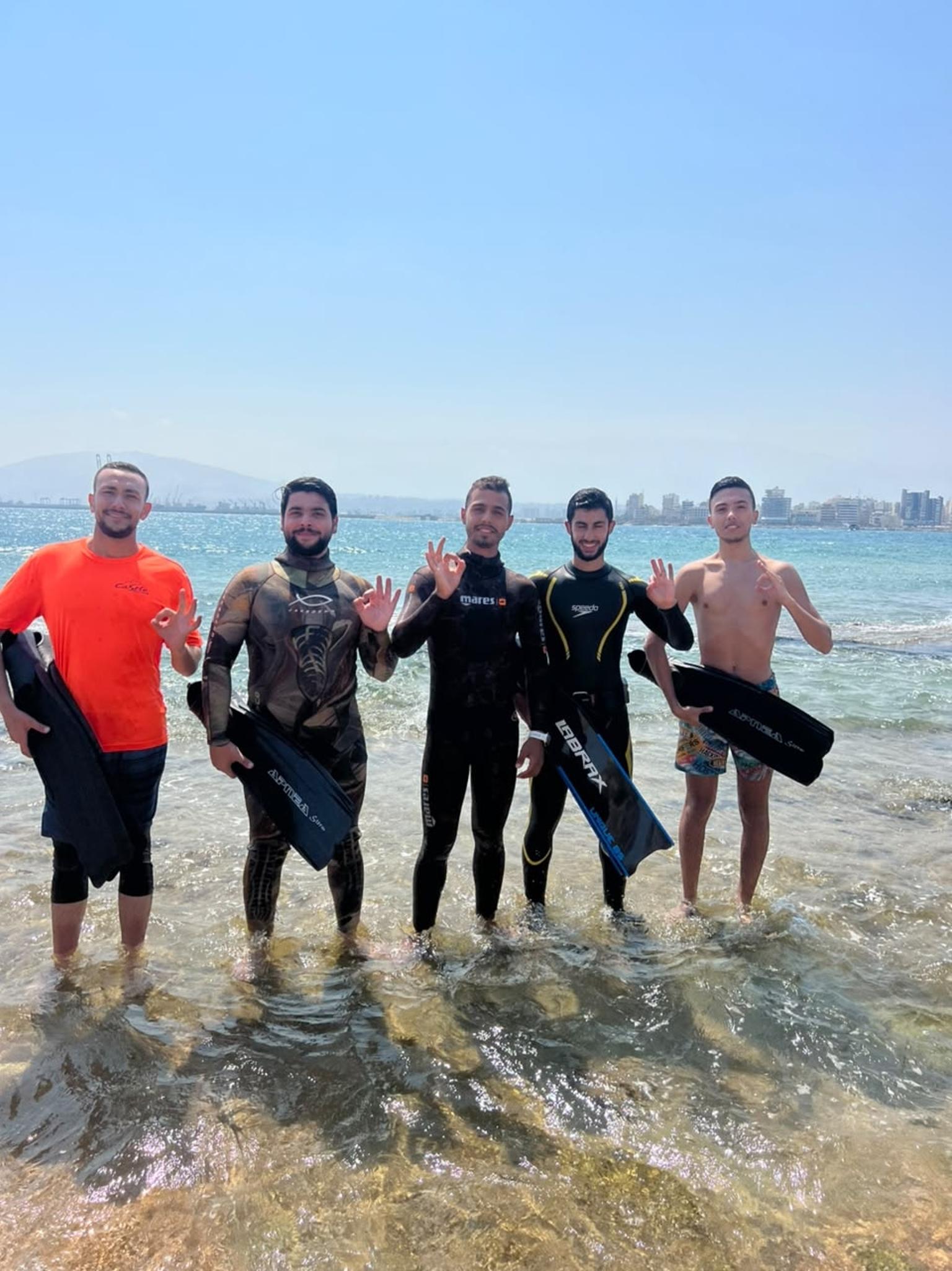 Spearfishers in camo wetsuits with their fins on the shore