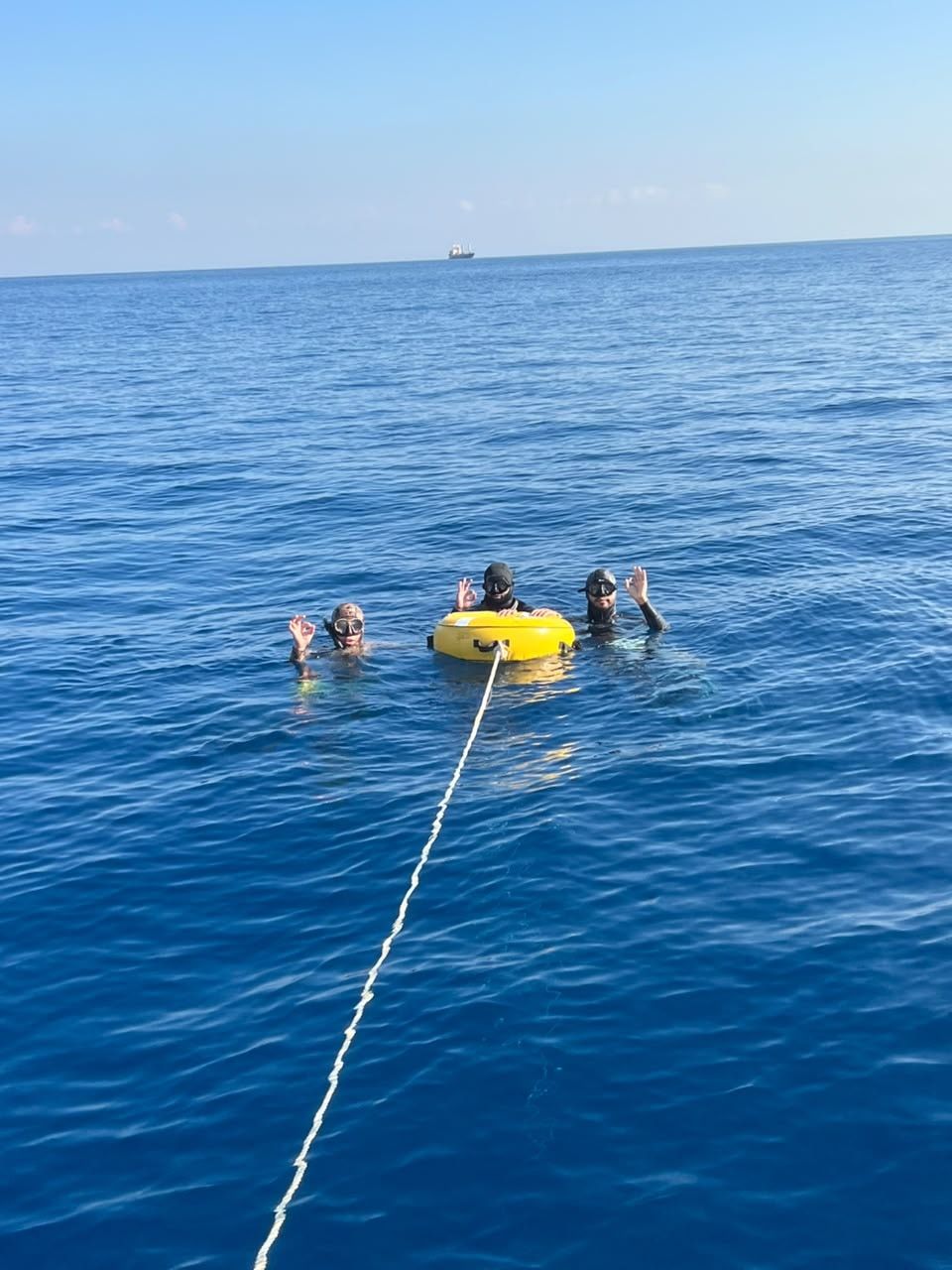Three freedivers around a yellow buoy in open water